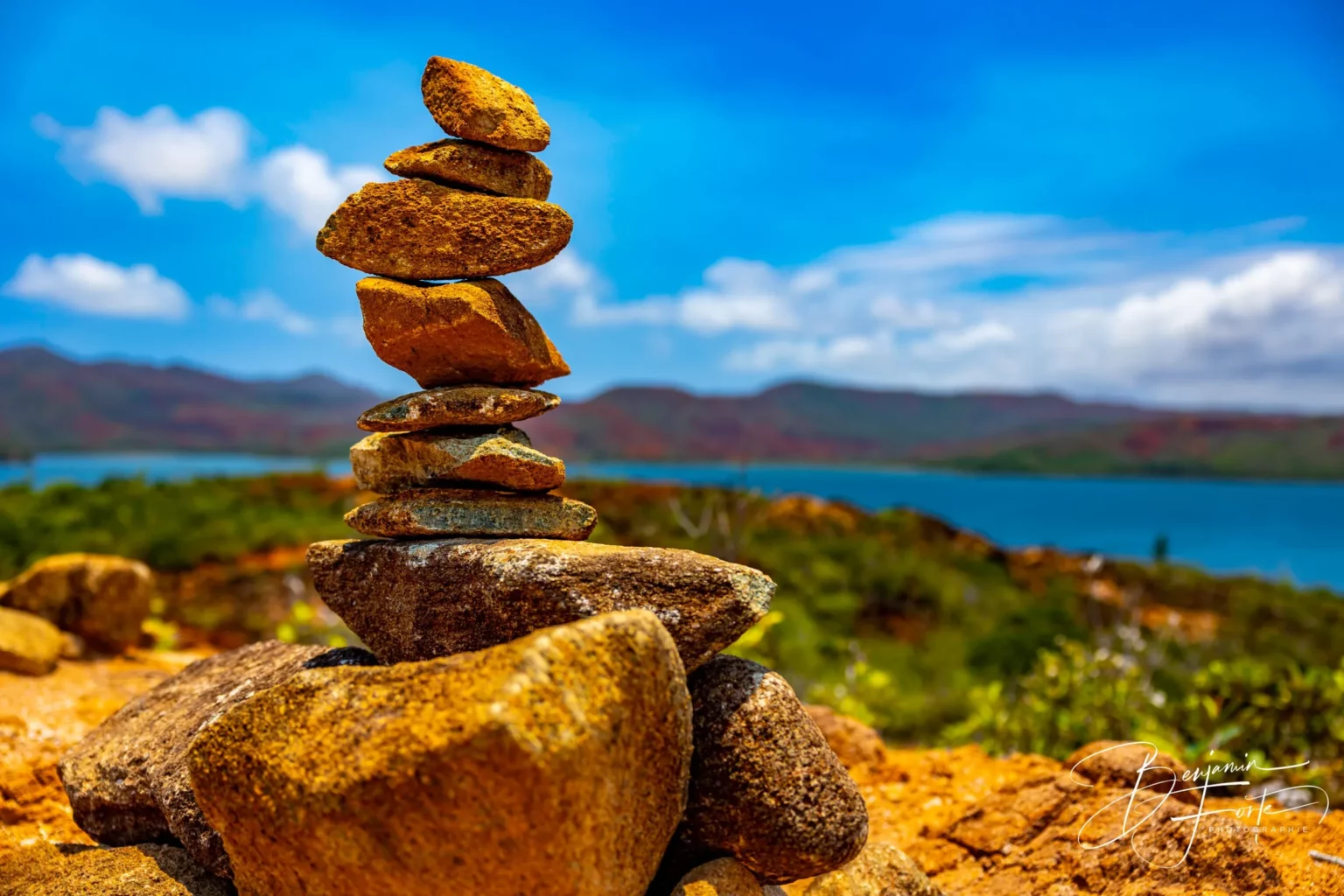 Un cairn de pierres empilées face au lagon, sur la terre rouge