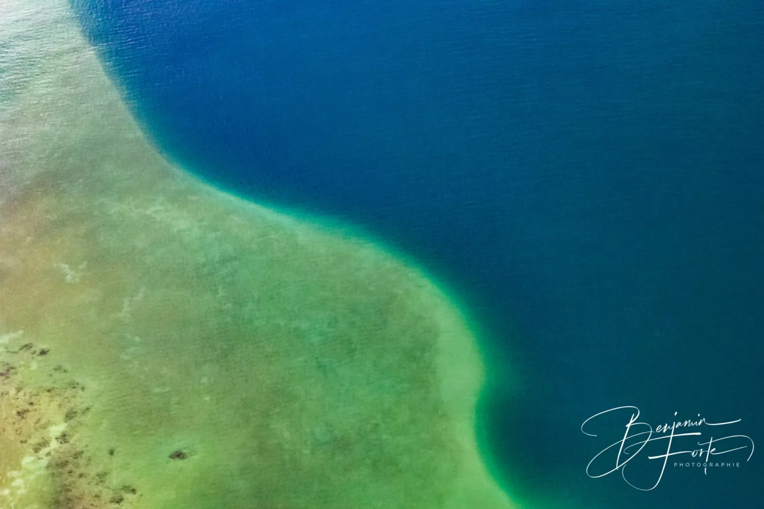 Vue aérienne de la limite entre un haut-fond turquoise et l’eau profonde du lagon