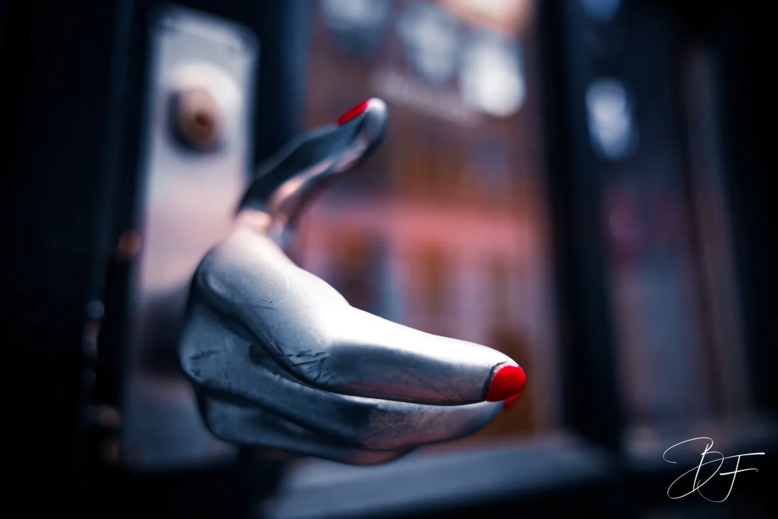 Une main sculptée en métal argenté, aux ongles rouges, tendue vers l’avant